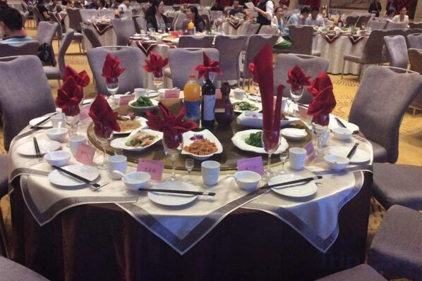 Una mesa de banquete dispuesta con platos, vasos y cubiertos, rodeada de sillas.
