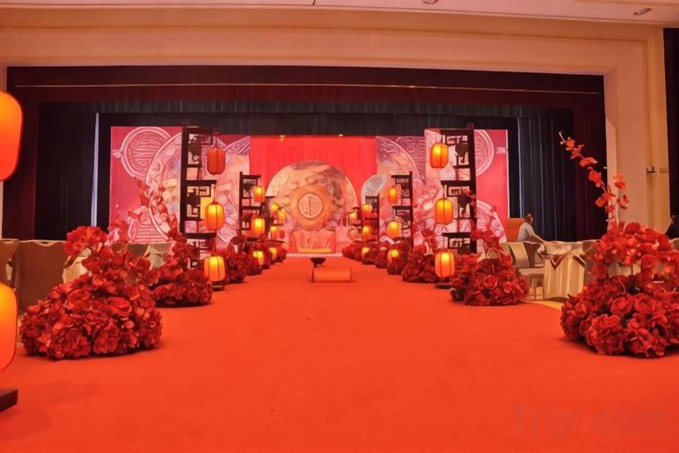 A stage with a red carpet, floral arrangements, and traditional lanterns.