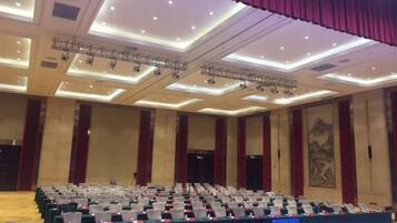 A conference room with rows of tables and chairs, a stage with lighting equipment, and a large mural on the wall.