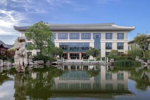 A traditional building with a modern glass facade, a pond with a stone sculpture, and a clear sky.