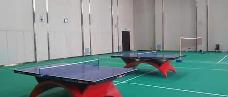 Two ping pong tables in a room with a green floor and white walls.