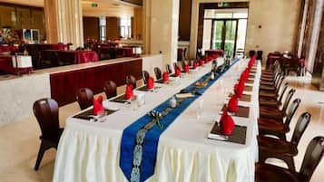 A long dining table with chairs, red napkins, and a blue table runner in a hotel dining area.