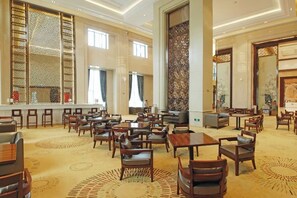 Un amplio hall de hotel con varias zonas de estar, un bar y grandes ventanales que dejan entrar luz natural.