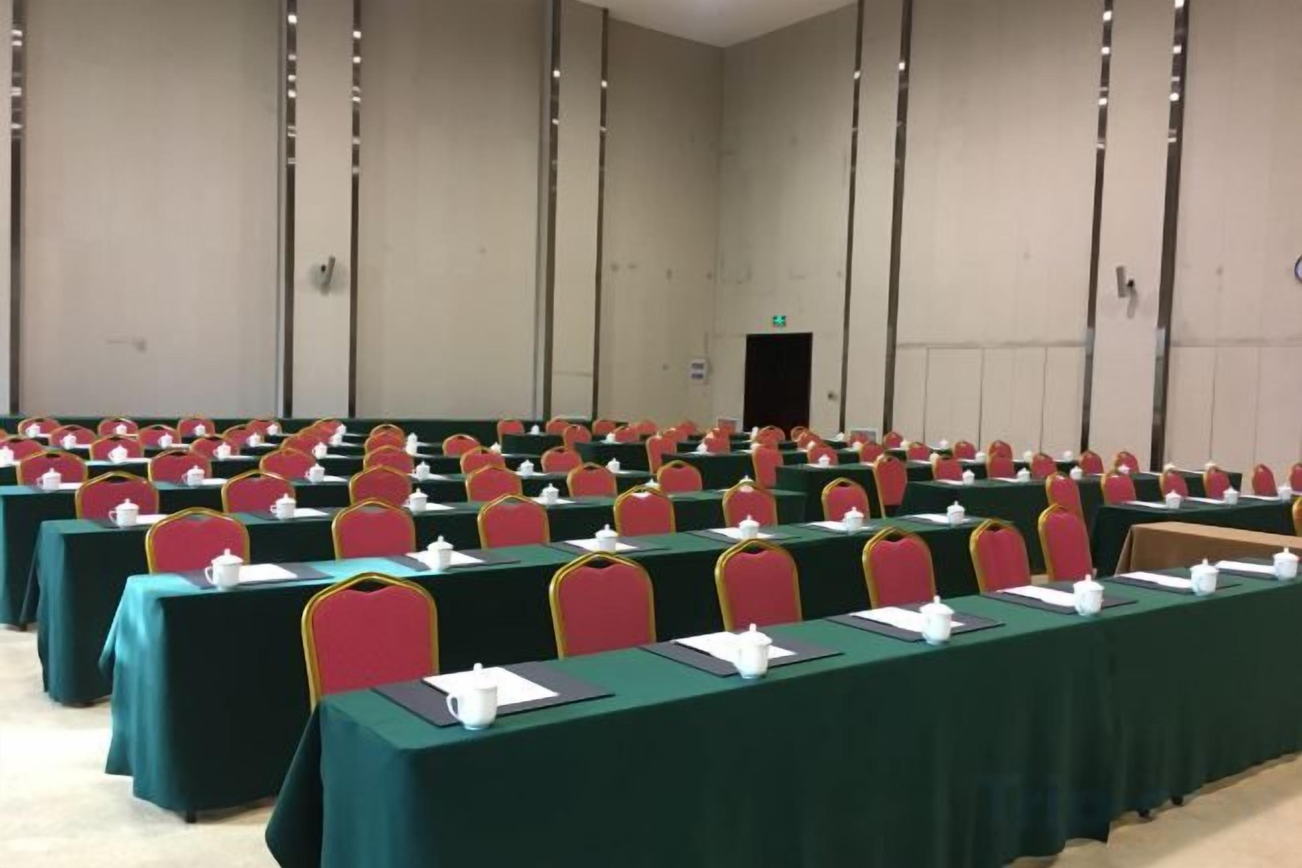 A conference room with rows of tables and chairs, a door in the background, and a plain wall.