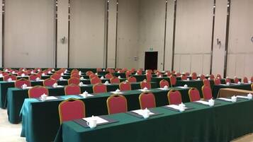 Una sala de conferencias con filas de mesas y sillas, una puerta al fondo y una pared lisa.