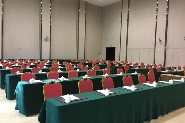 A conference room with rows of tables and chairs, a door in the background, and a plain wall.