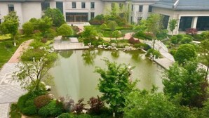 Un edificio de estilo tradicional con un estanque rodeado de jardines ajardinados y un puente.