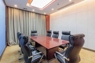 Un salón de conferencias con una mesa rectangular rodeada por seis sillas negras, un ventanal con cortinas y una pared con azulejos.