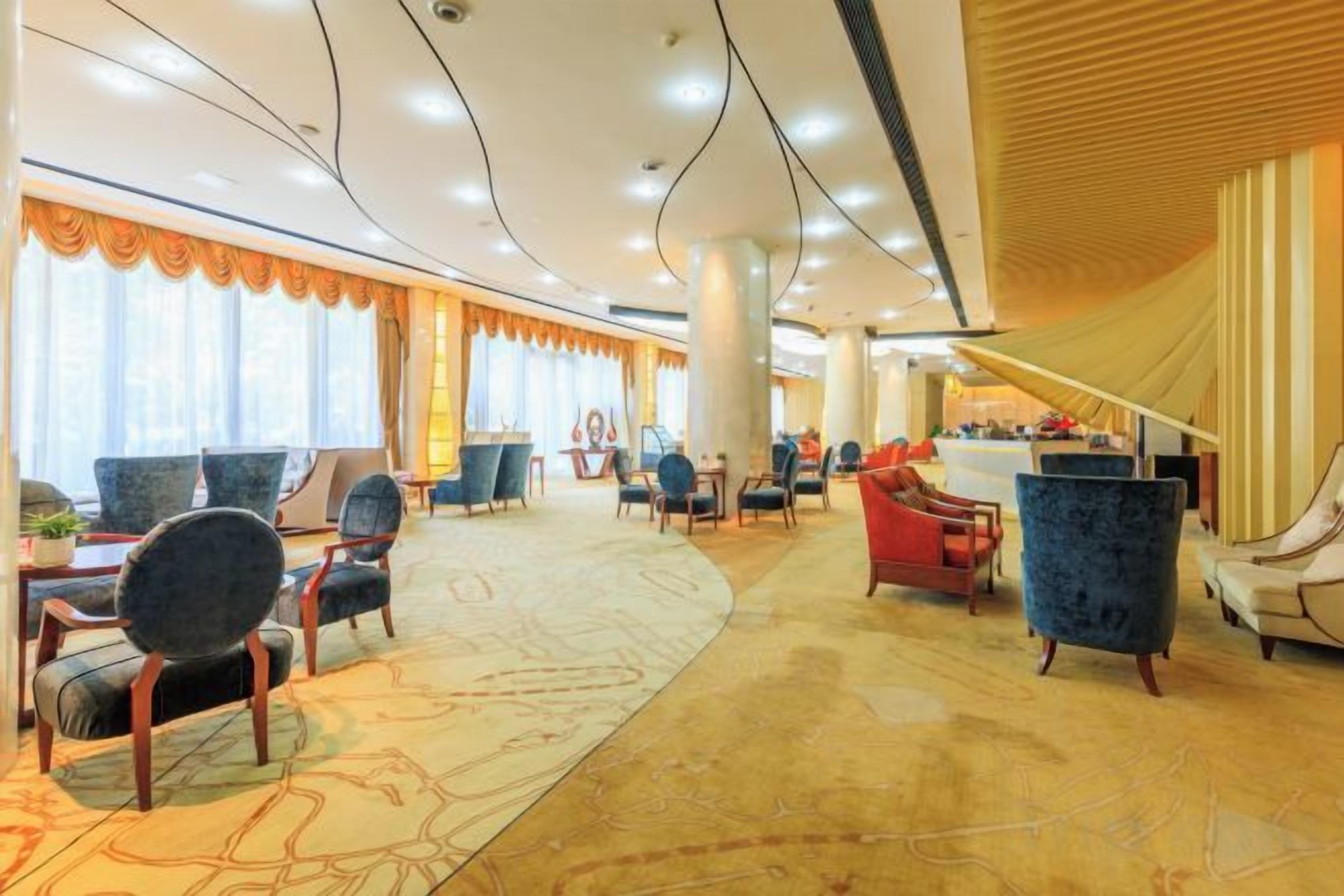 A hotel lobby with a curved ceiling, large windows with curtains, and a variety of seating arrangements including armchairs and sofas.