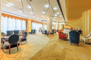 Un hall de hotel con techo curvo, ventanas amplias con cortinas y diversos tipos de asientos, incluyendo sillones y sofás.
