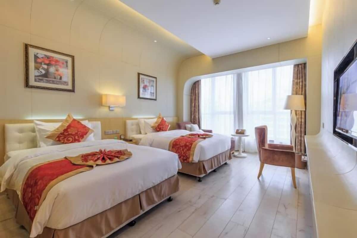 Habitación de hotel con dos camas, televisión, una silla y ventana con cortinas.