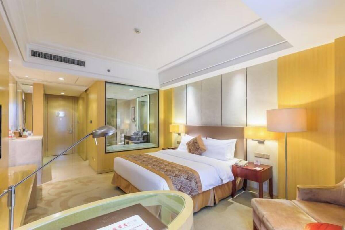 Habitación de hotel con cama, mesita de noche, lámpara y un aparador de vidrio.