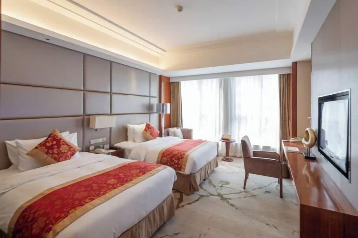 Habitación de hotel con dos camas, un escritorio, una silla, un televisor y un ventanal grande.