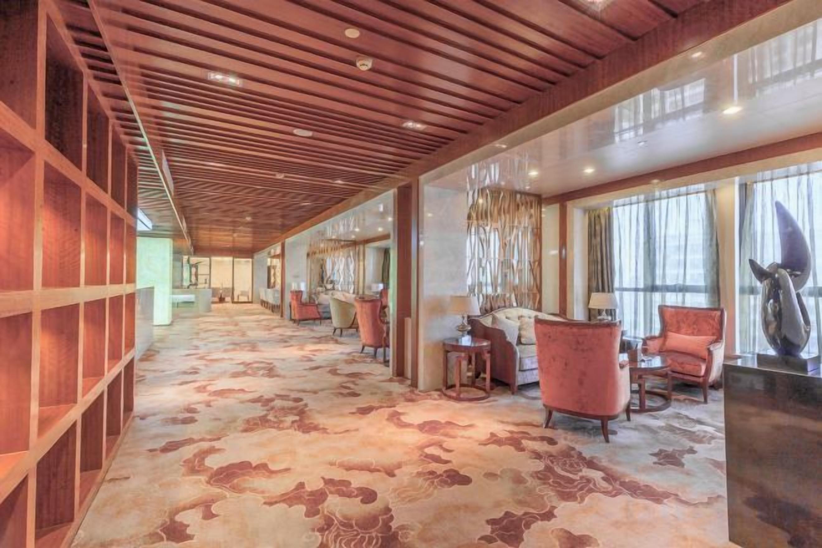 A hotel lobby with a patterned carpet, wooden paneling, and seating areas with chairs and tables.