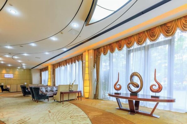 A hotel lobby with a curved ceiling, a reception desk, seating area, and large windows with curtains.