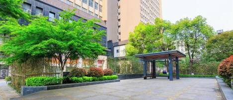 A courtyard with a gazebo, surrounded by greenery and tall buildings.