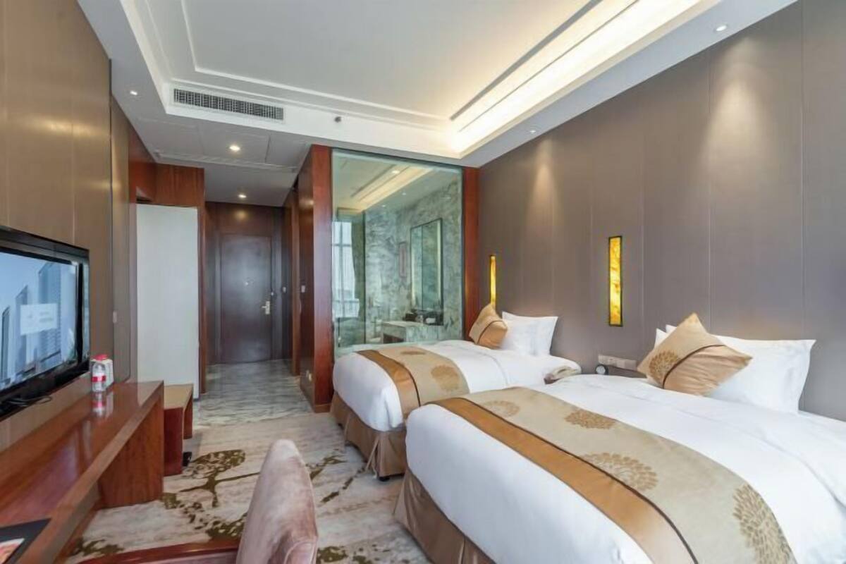 Habitación de hotel con dos camas, televisión, escritorio y espejo.