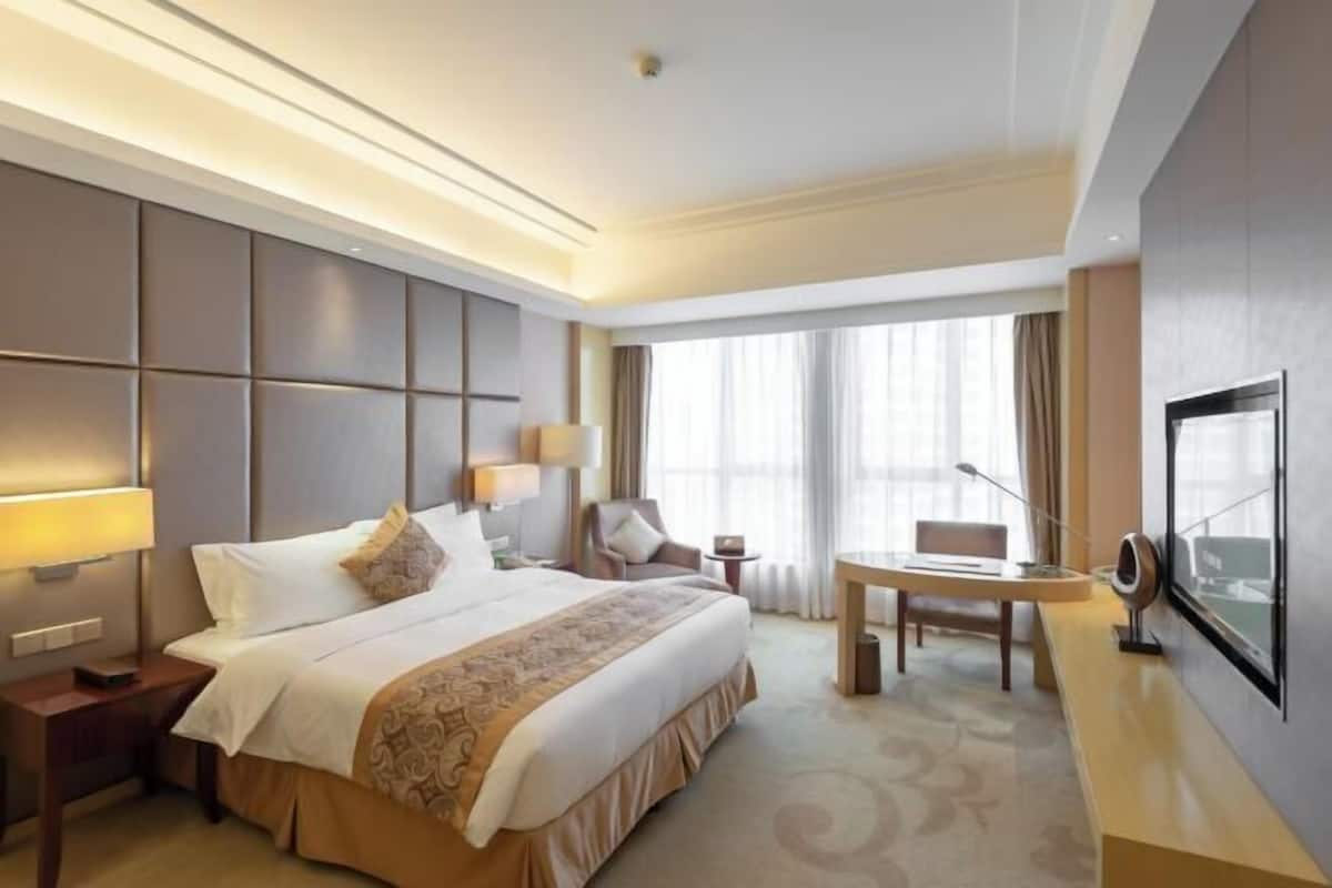 Habitación de hotel con una cama grande, mesitas de noche, escritorio, silla, televisor y ventana con cortinas.
