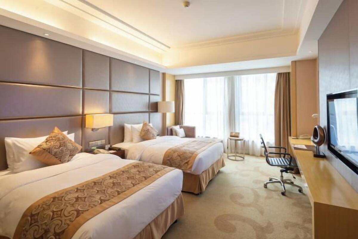 Habitación de hotel con dos camas, un escritorio, una silla, un televisor y una ventana con cortinas.