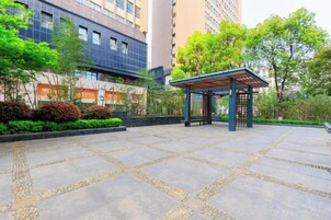 A courtyard with a pavilion, stone tiles, and greenery.