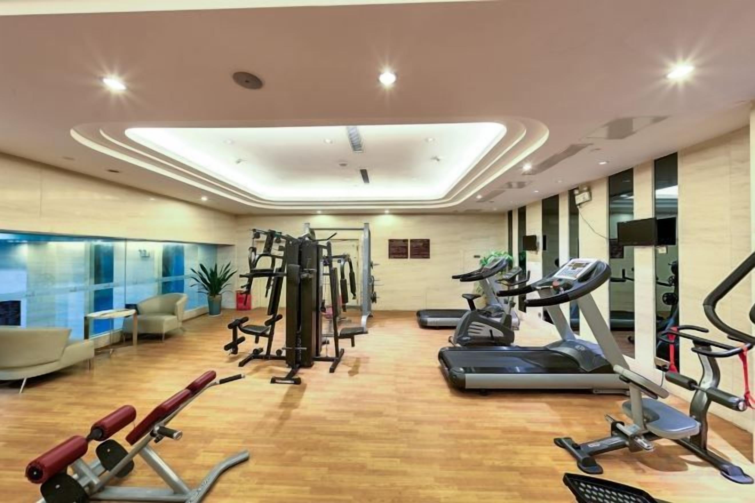 Een fitnessruimte met cardioapparatuur, gewichten en een spiegelwand.