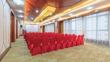 Un salón de conferencias con filas de sillas, un atril y ventanas amplias.