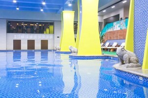 Una piscina interior con agua azul cristalina, pilares amarillos y una estatua de rana.