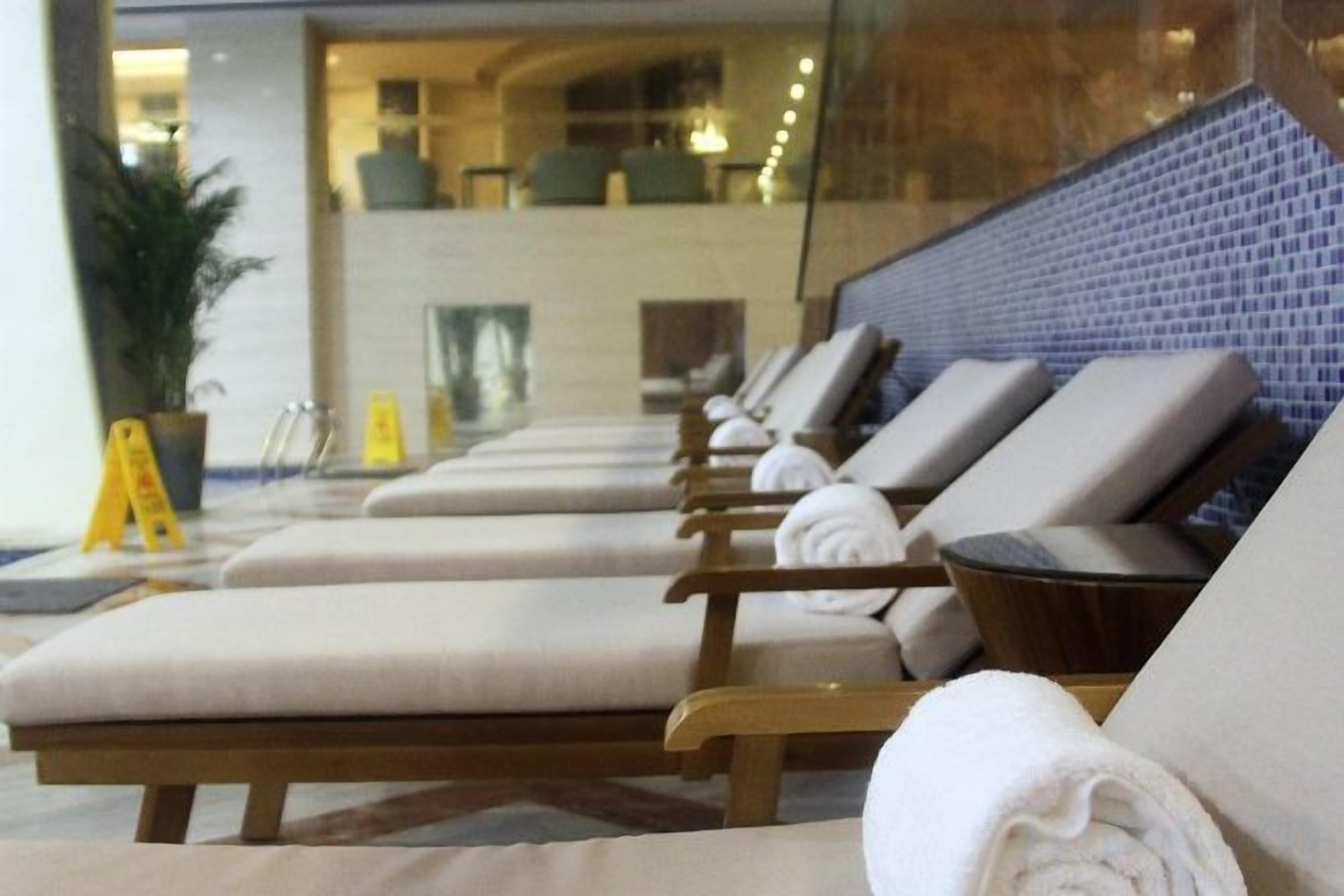 A row of sun loungers with towels, a potted plant, and a tiled wall in a hotel lobby.