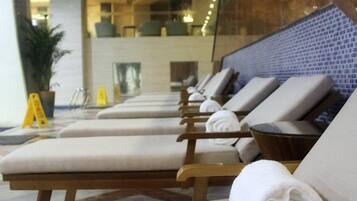 A row of sun loungers with towels, a potted plant, and a tiled wall in a hotel lobby.