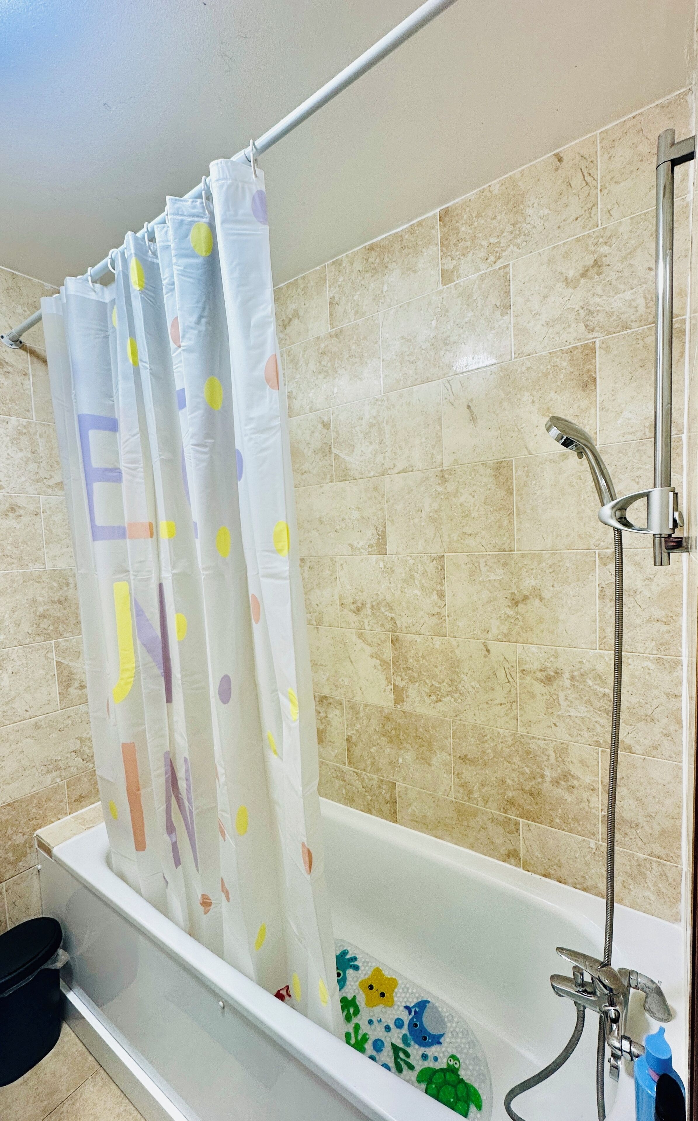 A bathroom with a bathtub, shower, and a curtain with colorful letters.