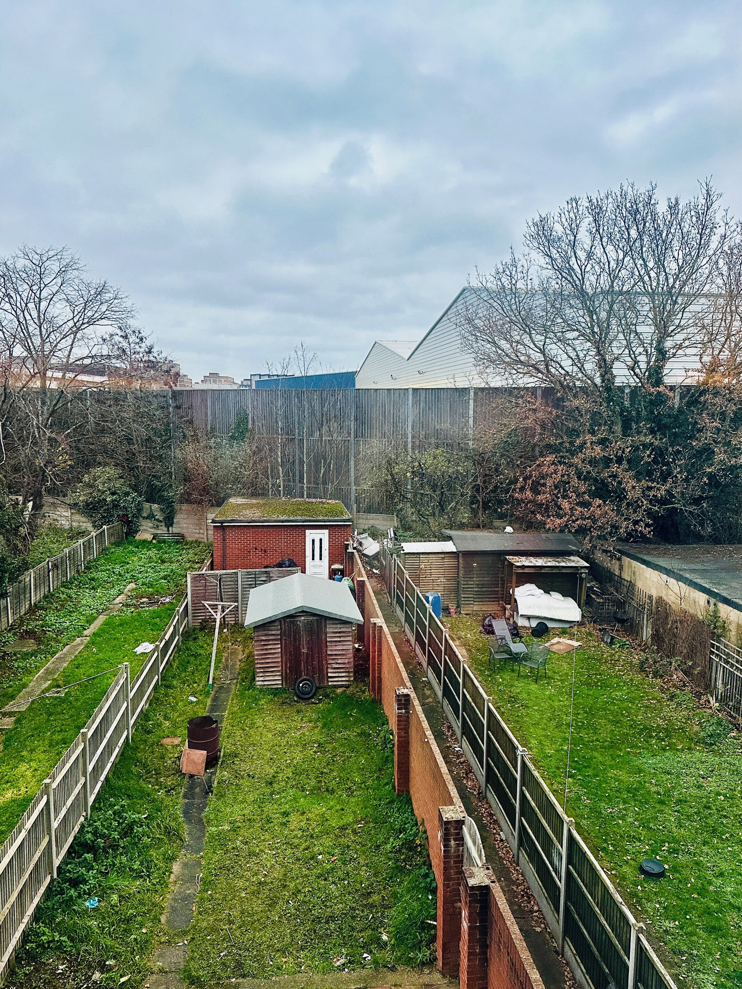 Une cour clôturée avec un petit abri, un bâtiment en briques et une zone herbeuse.