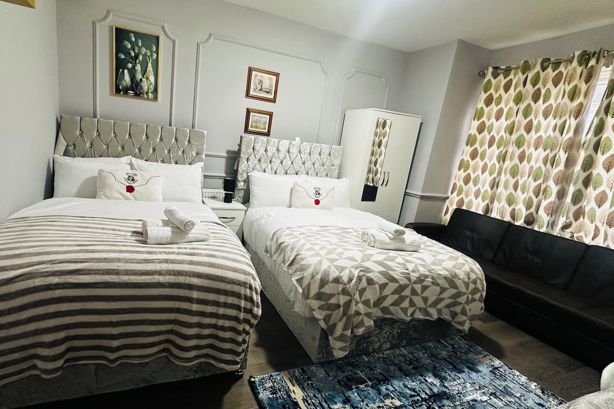A hotel room with two beds, a sofa, a patterned curtain, and artwork on the walls.