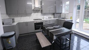 A modern kitchen with grey cabinets, a built-in microwave, a gas stove, and a dining table with a black and white patterned tablecloth. - Heathrow roomzzzz B&B (Hayes)