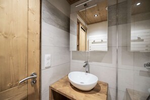 A bathroom with a wooden door, a white sink, a mirror, and a shower area. - Superb apartment for 4 people, 30m², 2 sleeping areas, renovated, at the foot of the slopes (VAL THORENS)