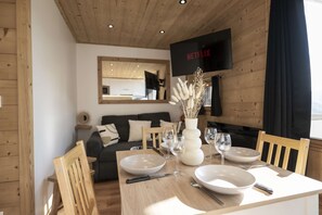 A dining area with a wooden table set for two, a mirror, a sofa, and a television displaying the Netflix logo. - Superb apartment for 4 people, 30m², 2 sleeping areas, renovated, at the foot of the slopes (VAL THORENS)