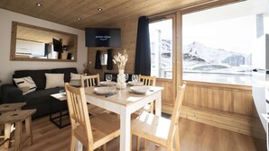 A modern interior with a dining area, wooden furniture, and a large window offering a view of a snowy landscape. - Superb apartment for 4 people, 30m², 2 sleeping areas, renovated, at the foot of the slopes (VAL THORENS)