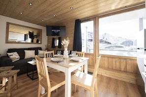 A modern interior with a dining area, wooden furniture, and a large window offering a view of a snowy landscape. - Superb apartment for 4 people, 30m², 2 sleeping areas, renovated, at the foot of the slopes (VAL THORENS)