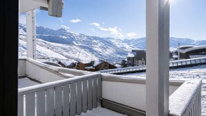 A balcony with a view of snow-covered mountains and a modern building in the background. - Superb apartment for 4 people, 30m², 2 sleeping areas, renovated, at the foot of the slopes (VAL THORENS)
