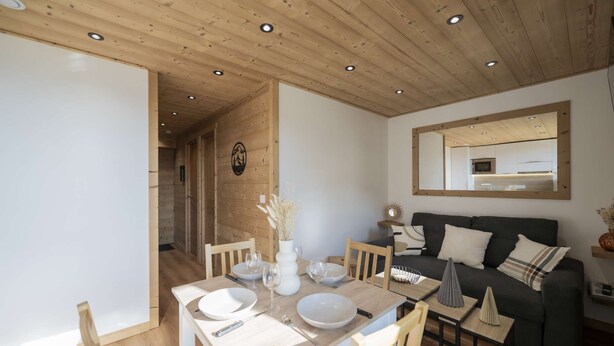 A modern interior with a dining area, a sofa, and a mirror. - Superb apartment for 4 people, 30m², 2 sleeping areas, renovated, at the foot of the slopes (VAL THORENS)