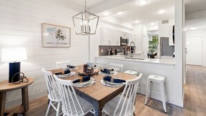 A modern kitchen with white cabinets, a central island, and a dining area with white chairs and a wooden table. - LUXURY 1st FLOOR VILLA / 2 BD 2BTH in Lely Resort (Naples)