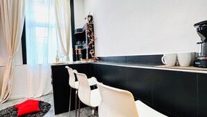 Una cocina moderna con encimera negra, sillas blancas y una cafetera.
