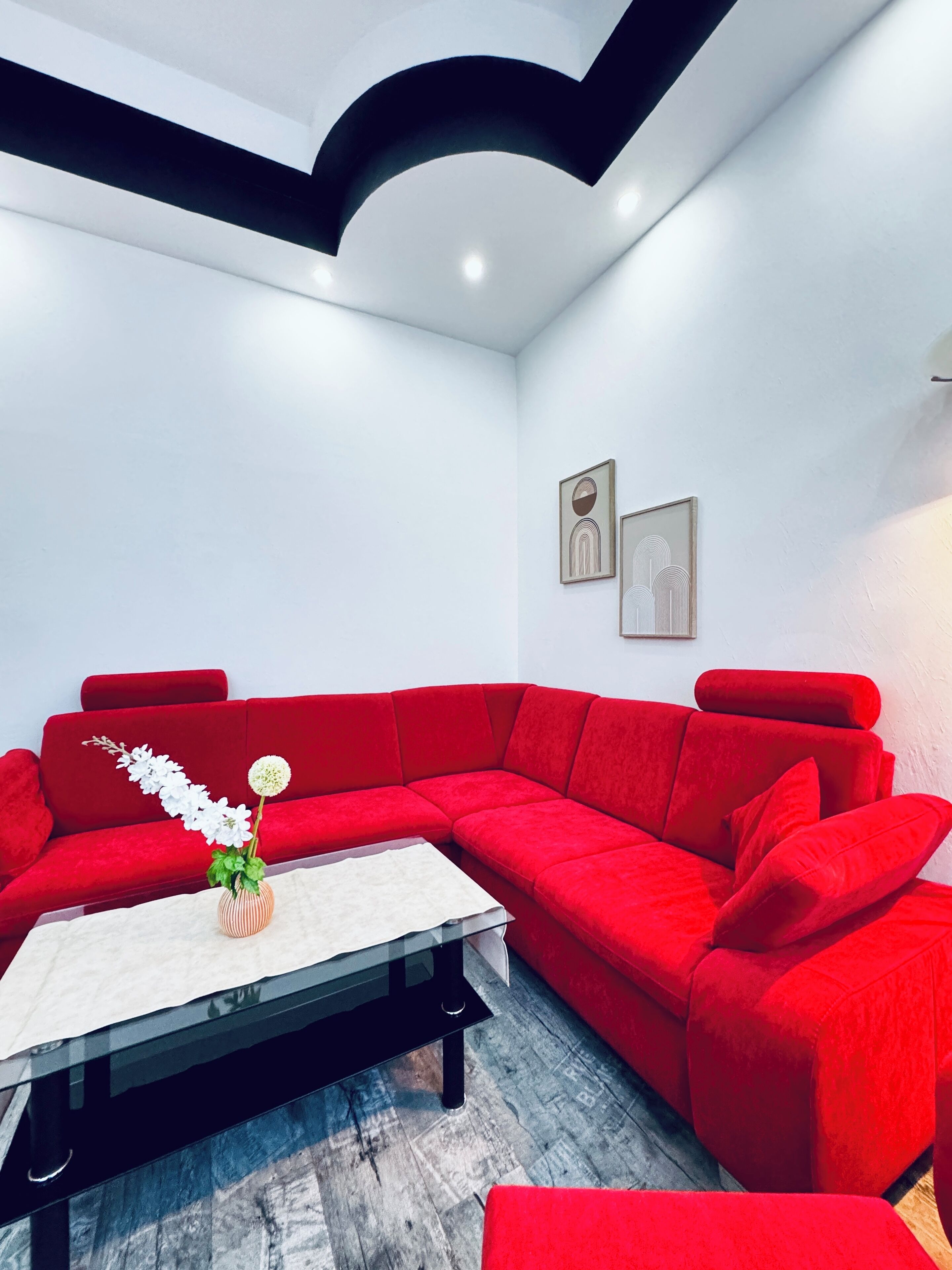 A modern living room with a red sectional sofa, a glass coffee table, and a vase with white flowers.