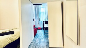 Un pasillo estrecho con una cama a la izquierda, un sofá rojo en el centro y una zona de comedor con sillas y una mesa al fondo.
