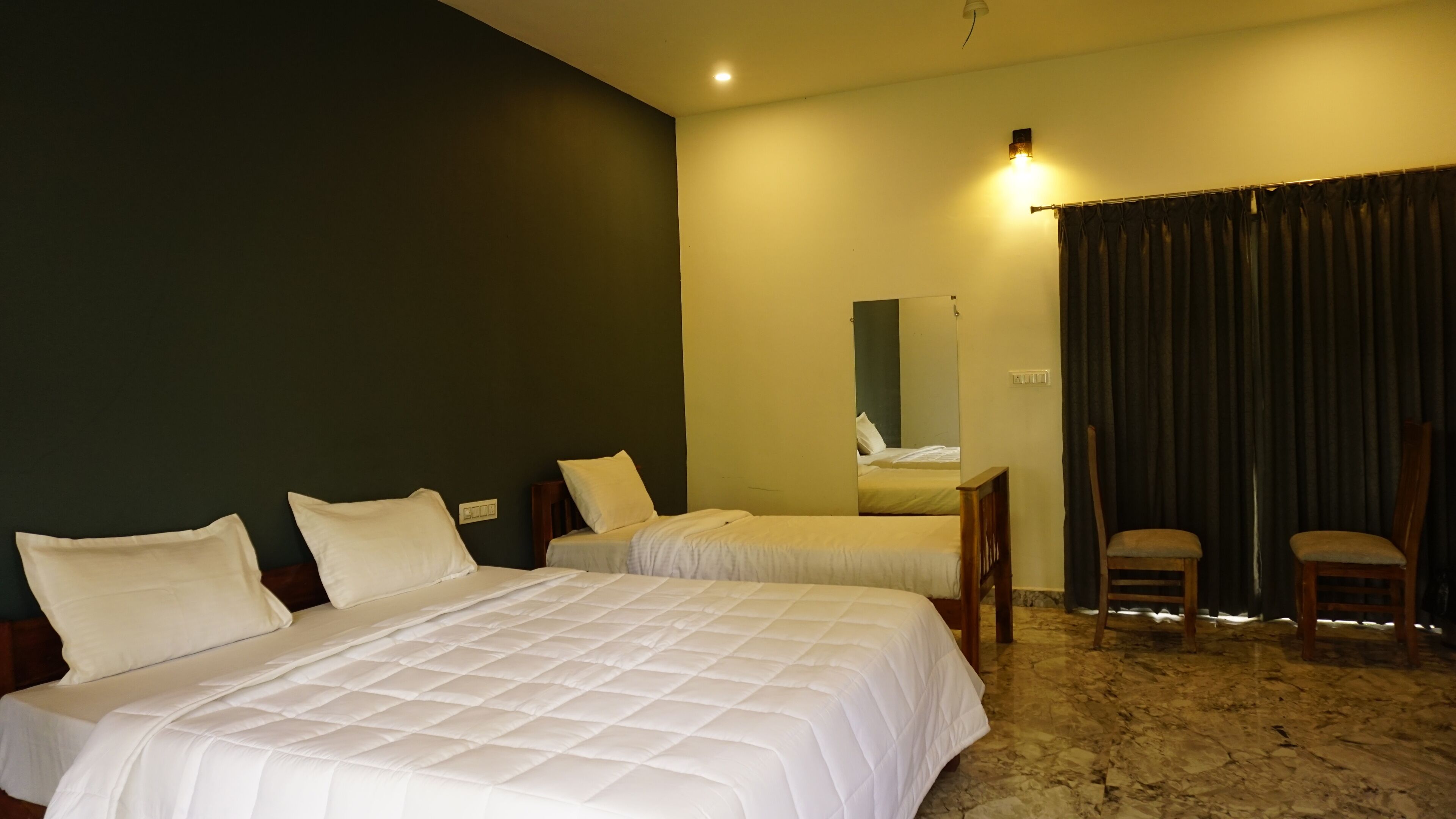 Ein Hotelzimmer mit zwei Betten, einem kleinen Tisch, zwei Stühlen, einem Spiegel und einem Vorhang.