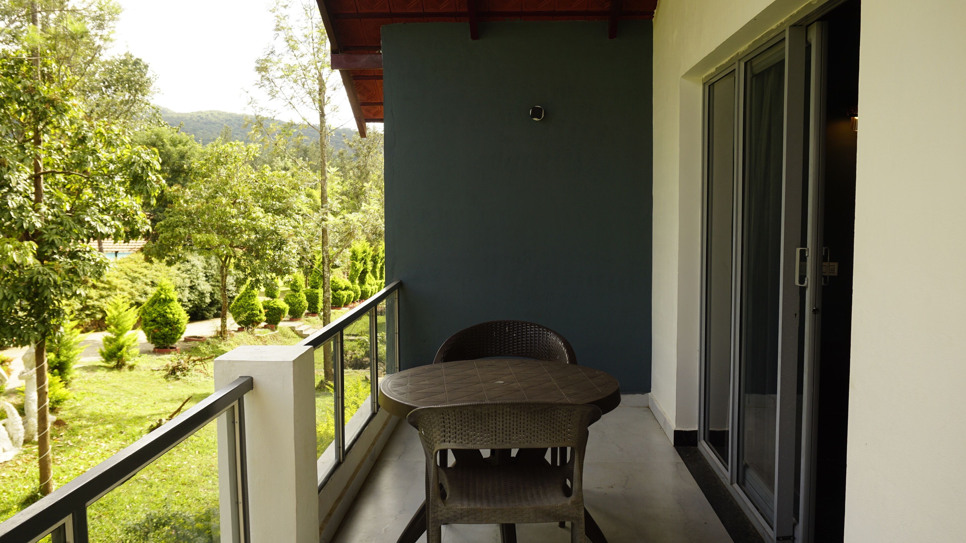 A balcony with a table and chairs, a view of a green landscape, and a door with a glass panel.