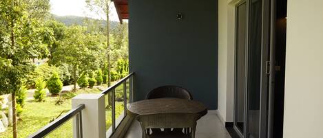 A balcony with a table and chairs, a view of a green landscape, and a door with a glass panel.