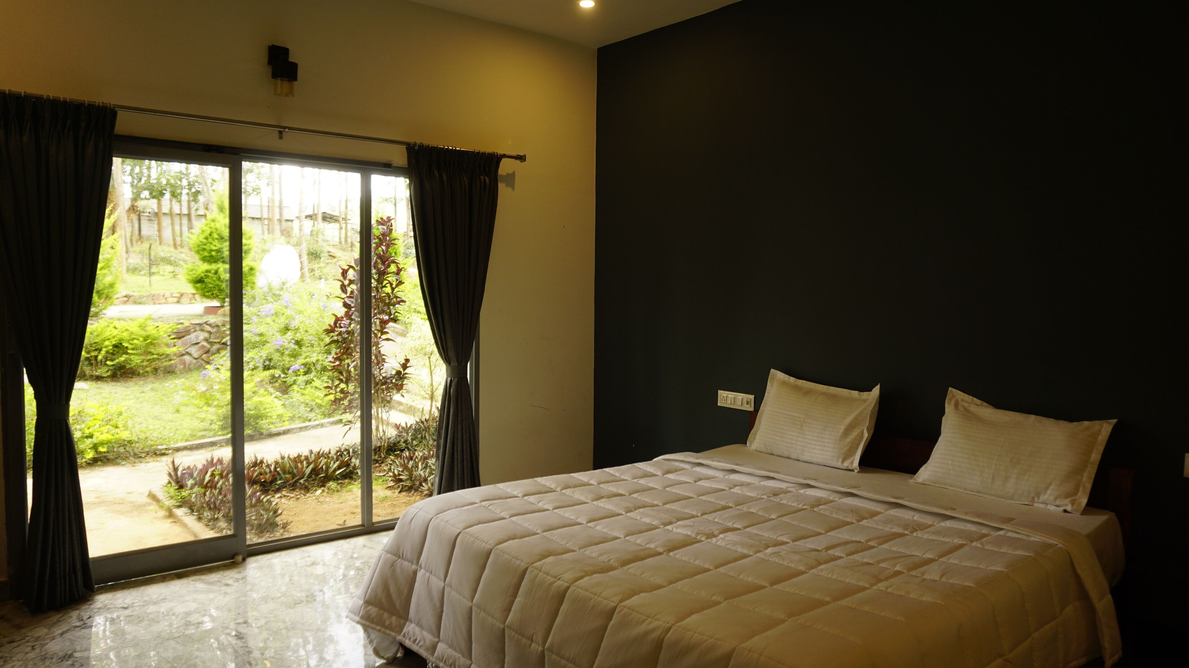 A bedroom with a large bed, a dark wall, and a sliding glass door leading to a garden.