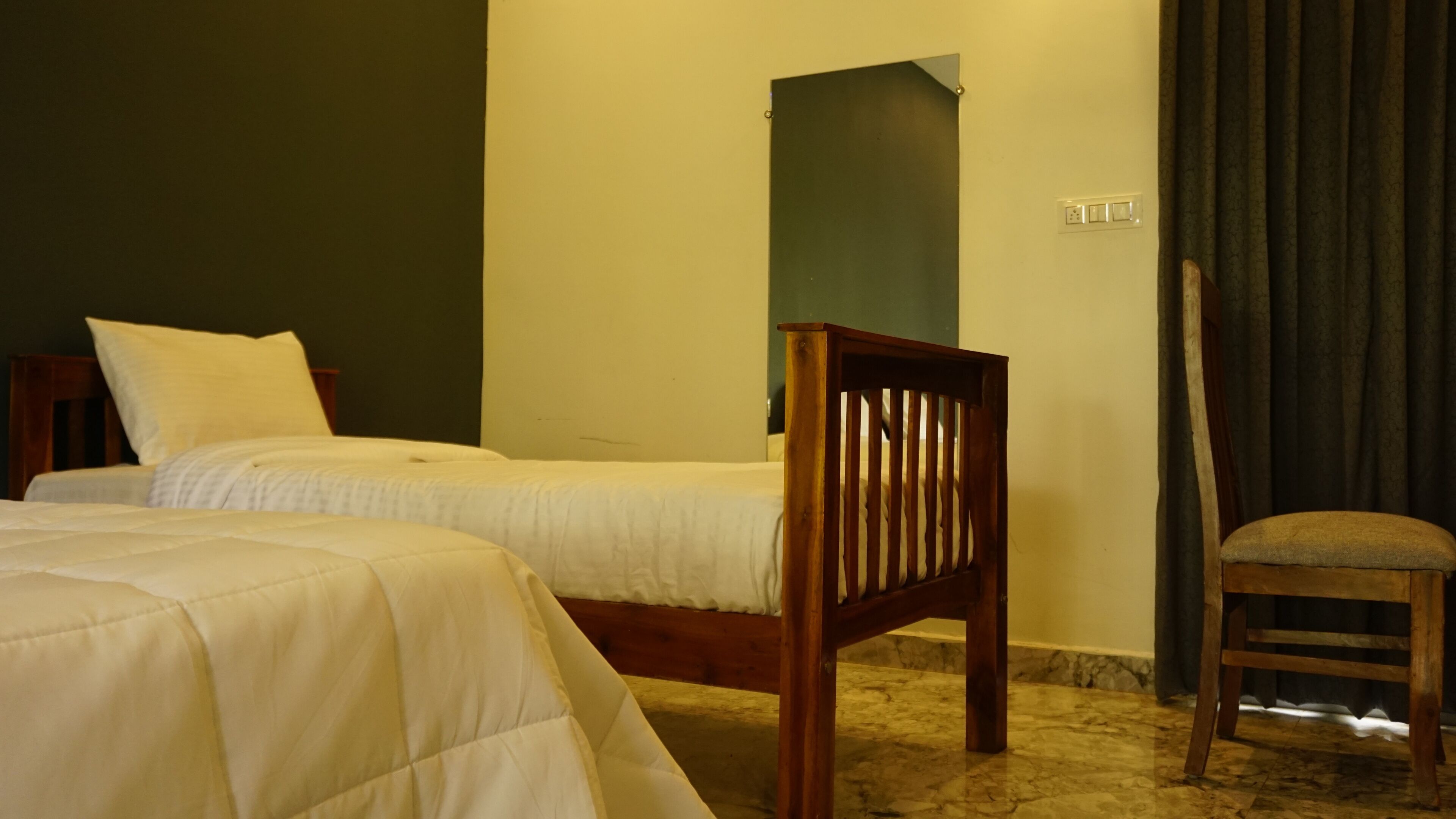A bedroom with two beds, a wooden chair, and a curtain.
