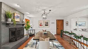 A dining area with a long table, a fireplace, and a staircase with a railing. - ICT Bunkhouse 2 King Beds, Family Friendly Retreat (Wichita)