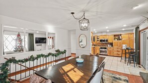 A modern kitchen with wooden cabinets, a dining area with a wooden table, and a Christmas tree by the window. - ICT Bunkhouse 2 King Beds, Family Friendly Retreat (Wichita)